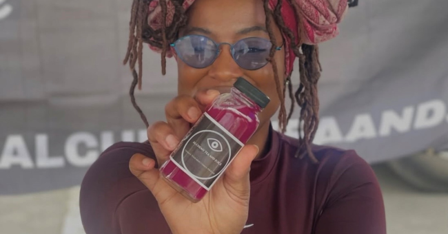 A person holds up a small bottle filled with purple liquid.