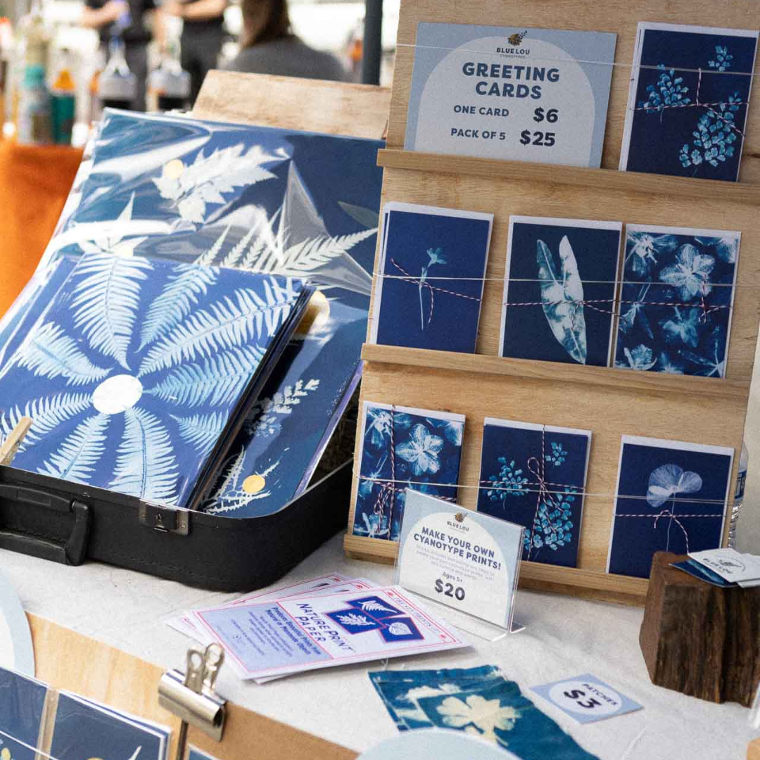 Display of Blue Lou Art cyanotype greeting cards, prints, and handmade goods at a market table.
