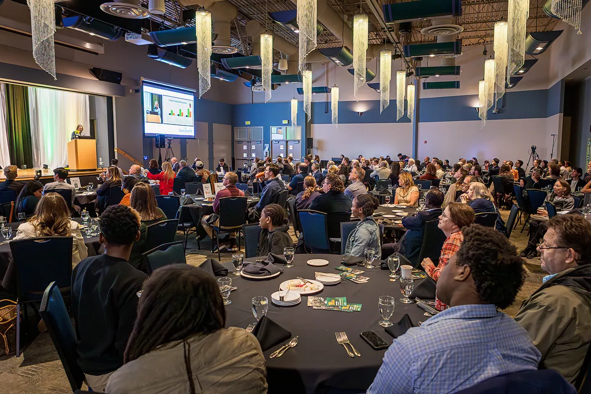 Audience members watching the IMPACT Pitch program in a large event room.