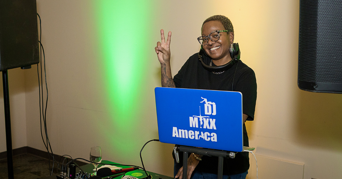 DJ MiXX America smiles and flashes a peace sign while providing music at the IMPACT Pitch event.
