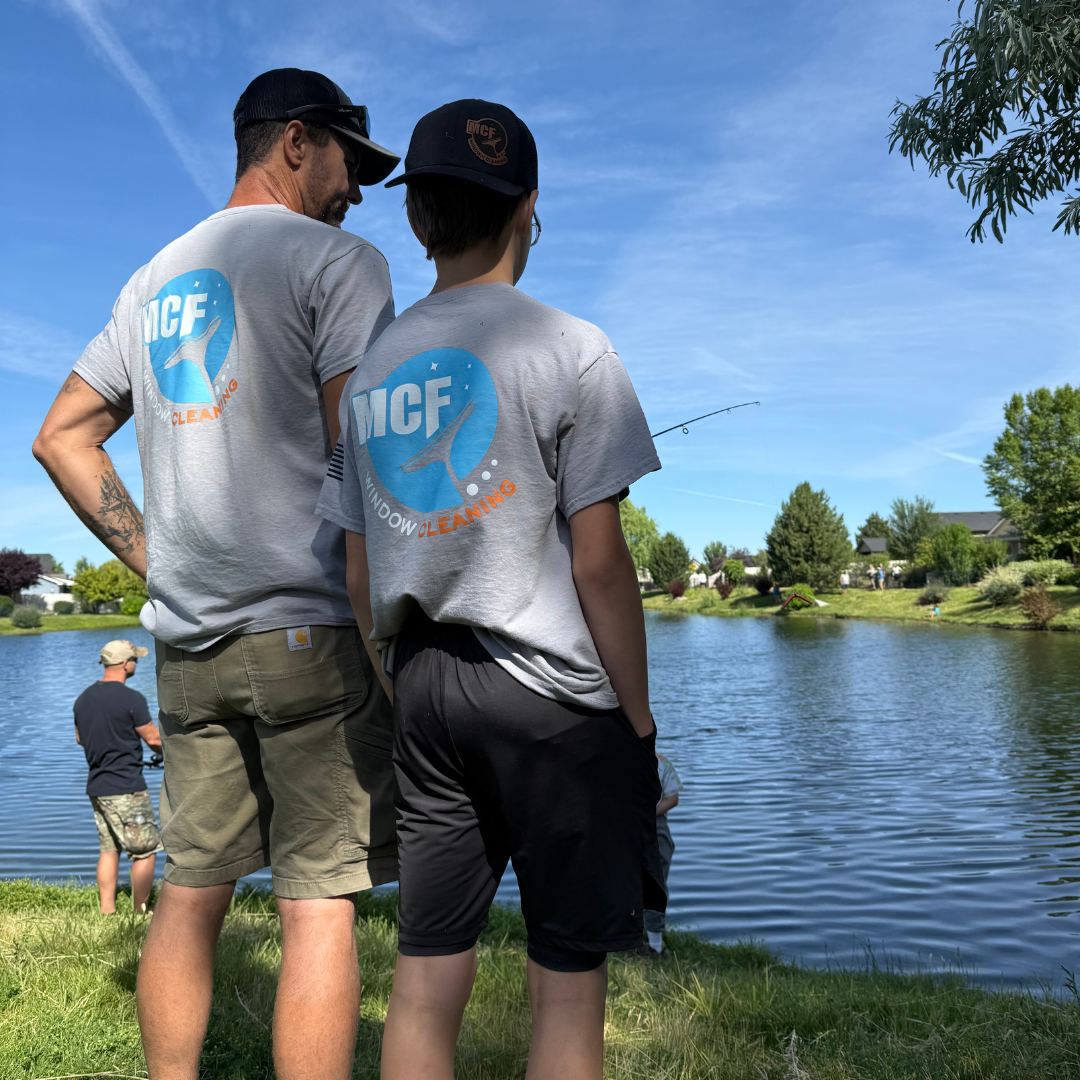 Two people wearing MCF Window Cleaning shirts standing beside a lake on a sunny day.