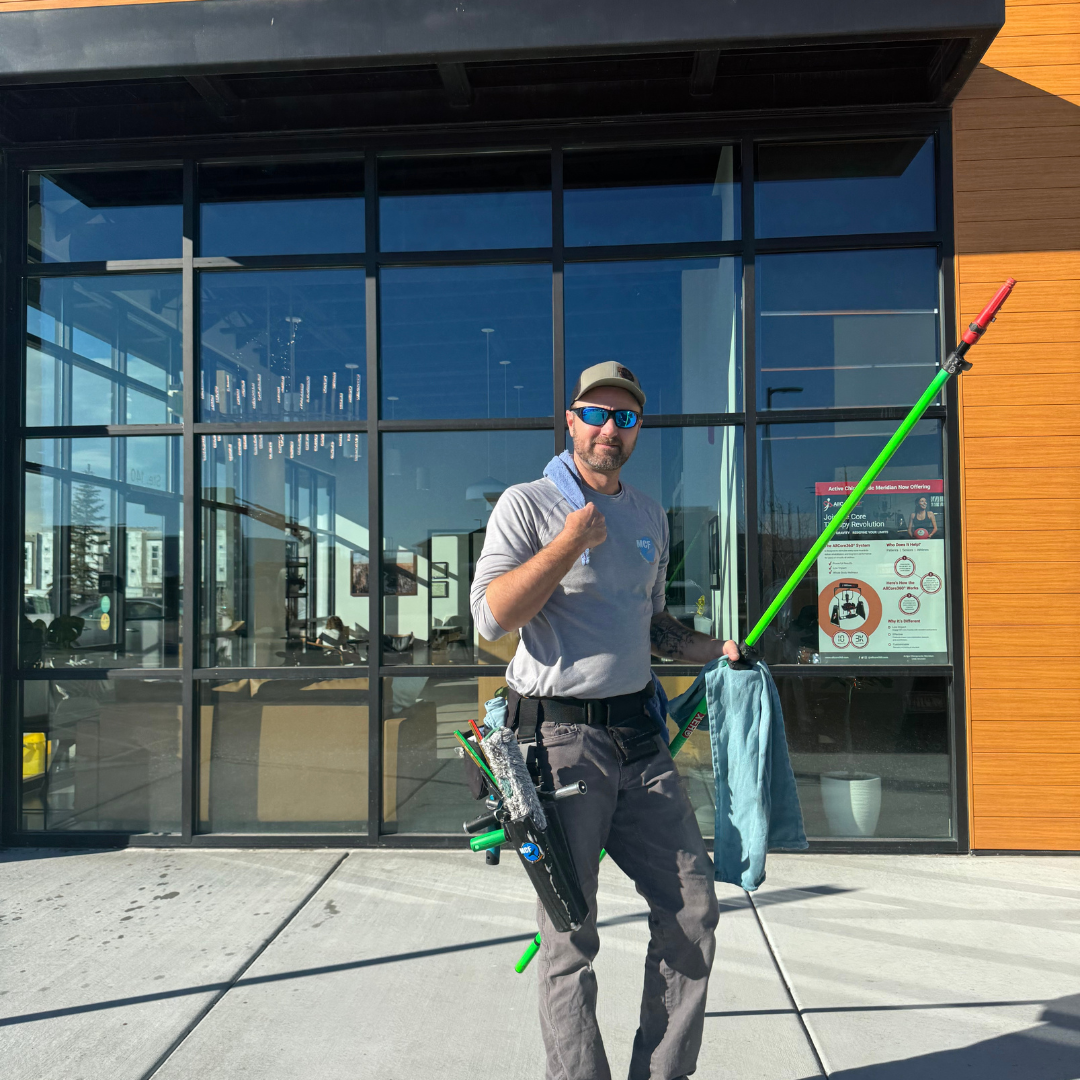MCF Window Cleaning technician standing with window-cleaning equipment outside a commercial building.