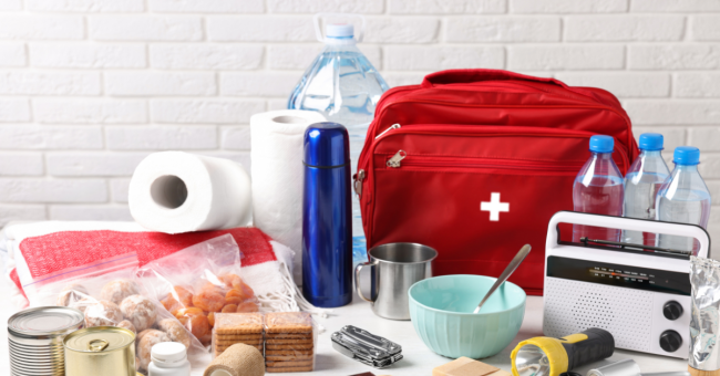 Emergency preparedness supplies including a first aid kit, flashlight, water, and other essentials arranged on a table.