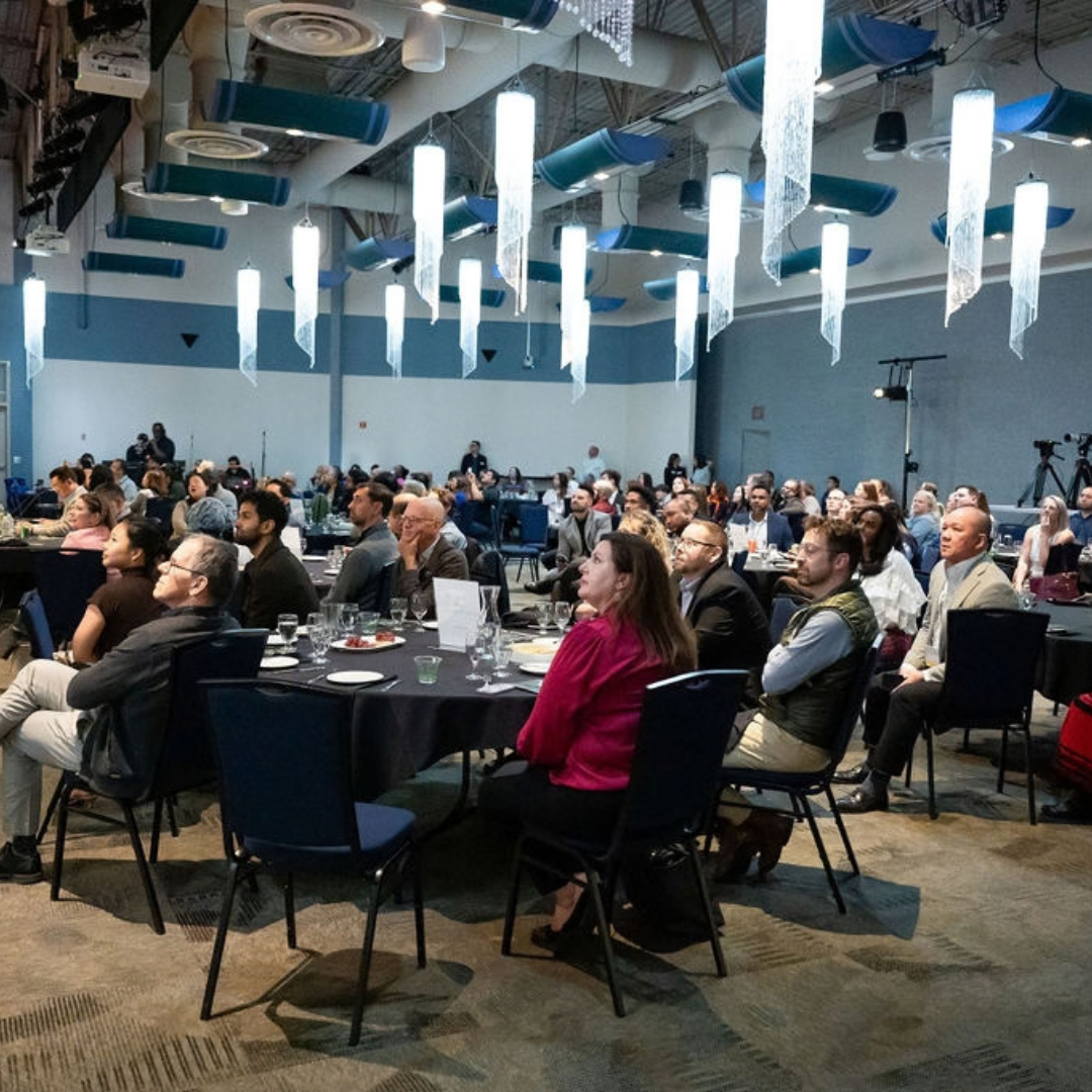 Attendees seated at tables watch the IMPACT Pitch 2026 final competition at South Seattle College.