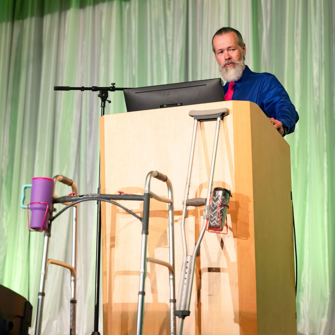 Joshua Yocum of Crutch Carries presents onstage with mobility devices displaying his drink-holder product.